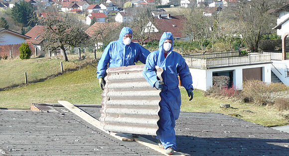 Männer in Schutzanzügen tragen eine Dachplatte