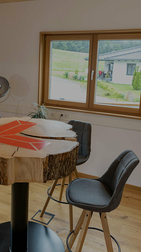 Tisch aus Holzstamm mit dem Logo der Zimmerei Luger und vier Stühle in einem Raum
